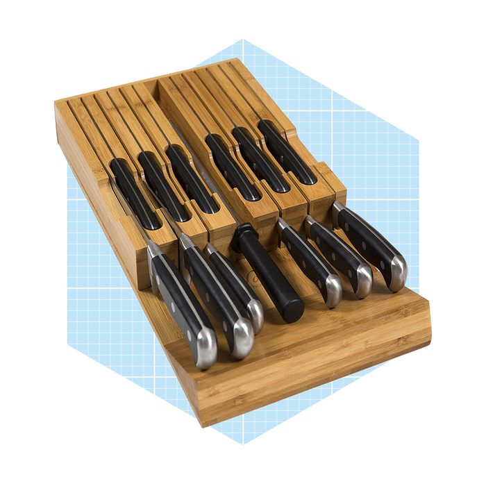 A bamboo knife block holds several kitchen knives with black handles, arranged neatly in slots, against a light blue grid background.