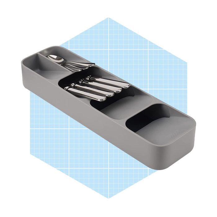 A gray cutlery tray holds several stainless steel utensils, organized in compartments, set against a light blue grid background.