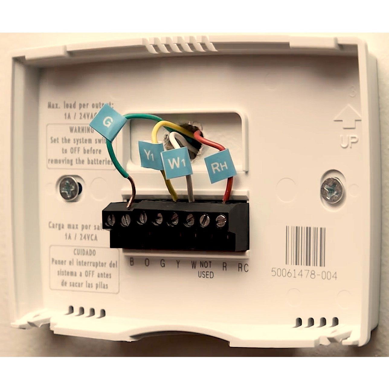 A thermostat mounted on a wall shows colored wires connected to labeled terminals. Nearby, instructions caution to turn off the system before battery removal.