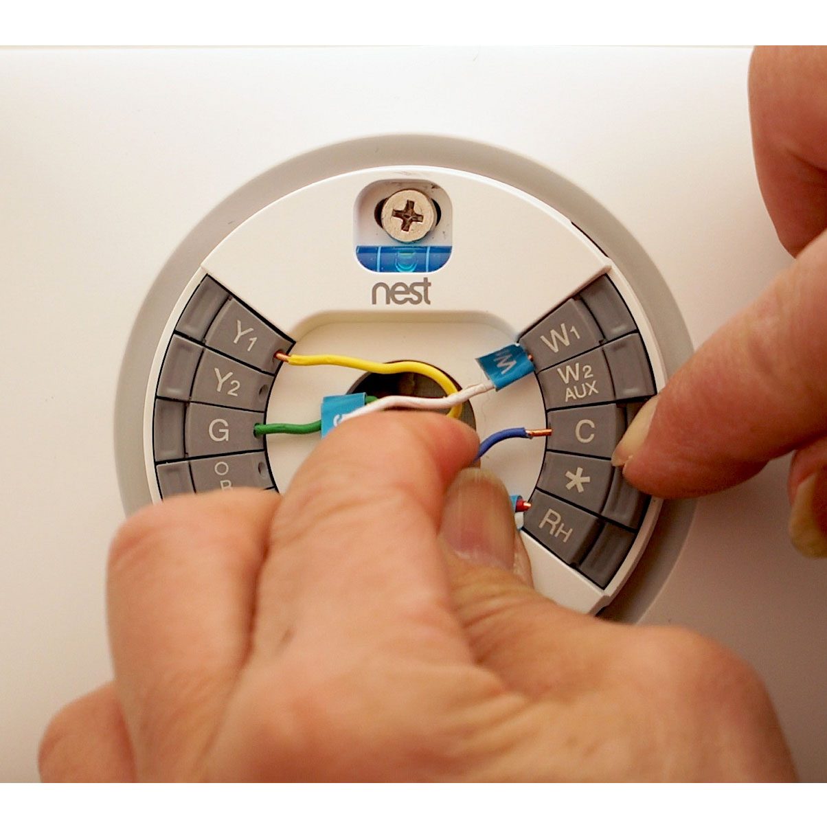 A person connects colored wires to a thermostat's labeled terminals, indicating installation or maintenance in a residential environment.