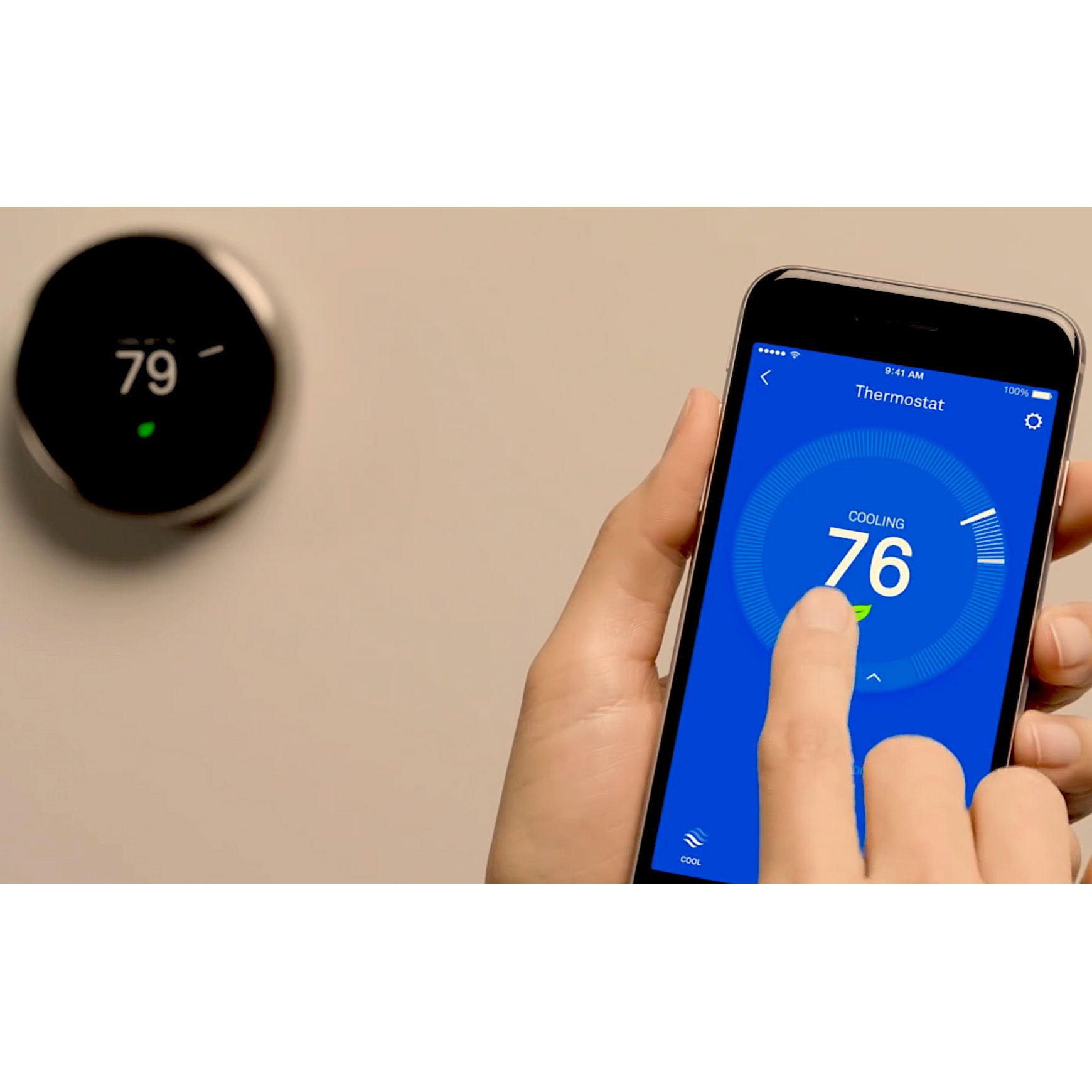 A hand adjusts the temperature on a smartphone app, displaying "COOLING 76," while a wall-mounted thermostat shows "79" in a modern indoor setting.