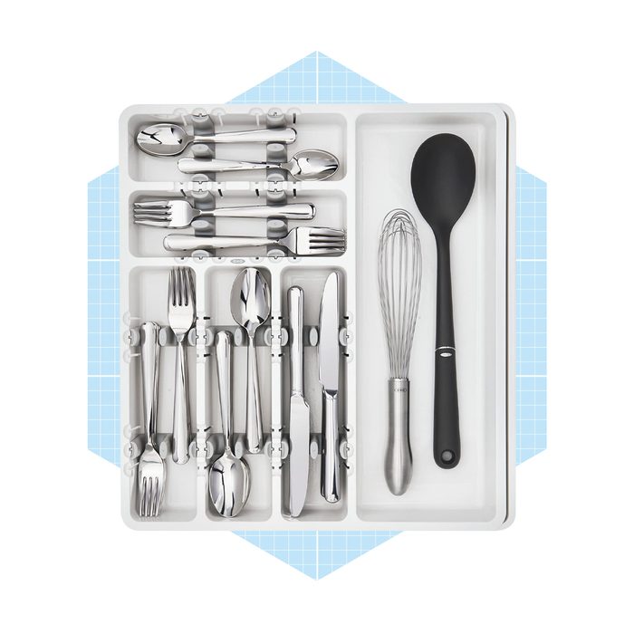 A cutlery tray displays various utensils, including spoons, forks, knives, a whisk, and a black spatula, organized neatly within a light-colored container.