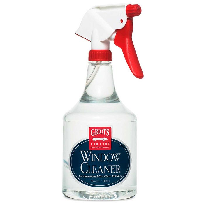 A clear spray bottle with a red trigger nozzle holds window cleaner, labeled for producing haze-free, ultra-clear windows, positioned against a neutral background.