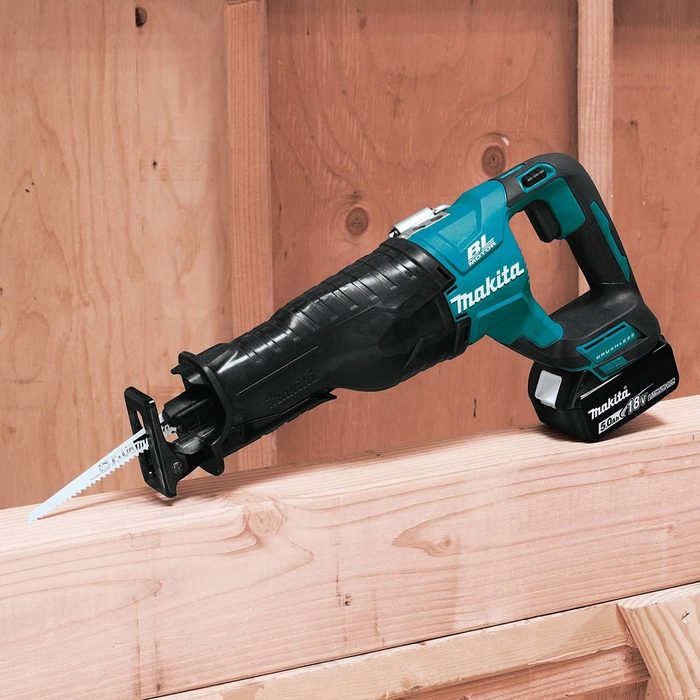 A reciprocating saw rests on a wooden beam, poised for cutting. Its blade is prominently displayed, surrounded by a backdrop of textured wooden boards.