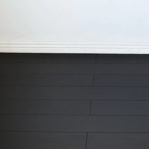 Dark wood flooring meets a white wall, creating a clean, minimalist transition at the base with subtle grooves along the wall's edge.