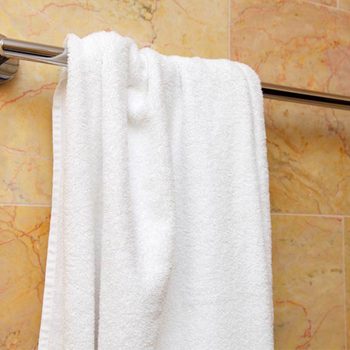 A white towel hangs on a silver rod against a textured, light-colored tiled wall, suggesting a bathroom environment.