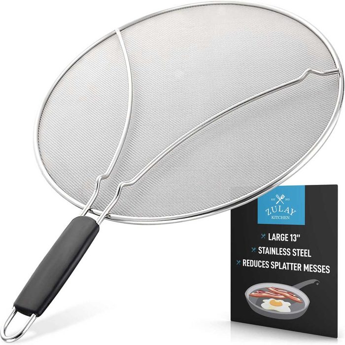 A large stainless steel splatter guard rests atop a black-backed label, showcasing its purpose of reducing kitchen messes while cooking.