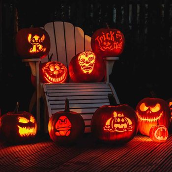 Illuminated carved pumpkins display various designs, including characters and skulls, arranged around a white chair on a dimly lit porch.