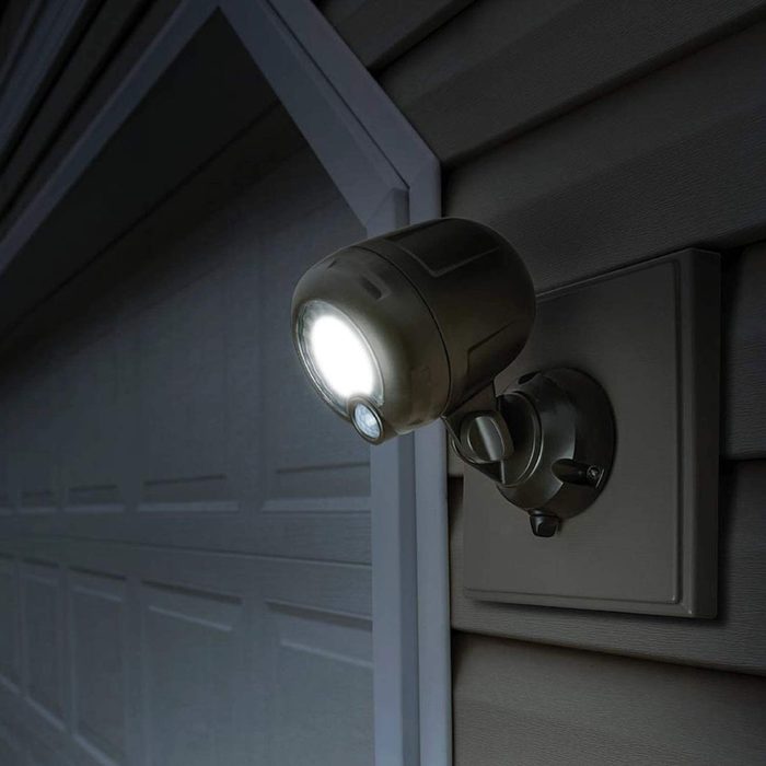 A mounted security light illuminates an entryway, highlighting a textured wall and a closed garage door in a dimly lit setting.