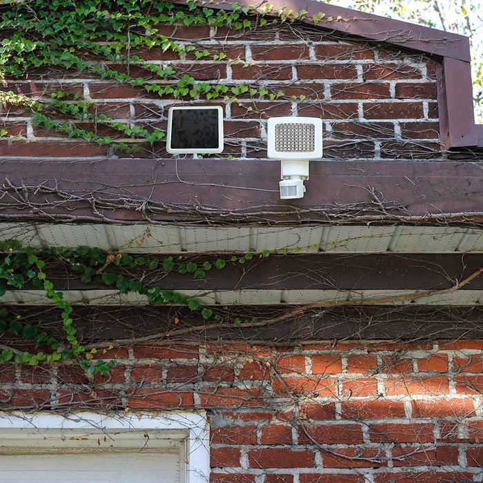 Two outdoor lights are mounted on a brown eave, surrounded by brick and green ivy climbing the wall, indicating a residential setting.