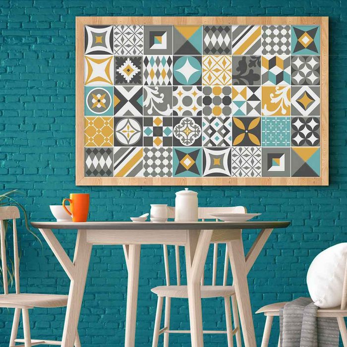 A colorful geometric patterned artwork hangs above a light wooden table set with orange and white cups in a teal-bricked dining area.