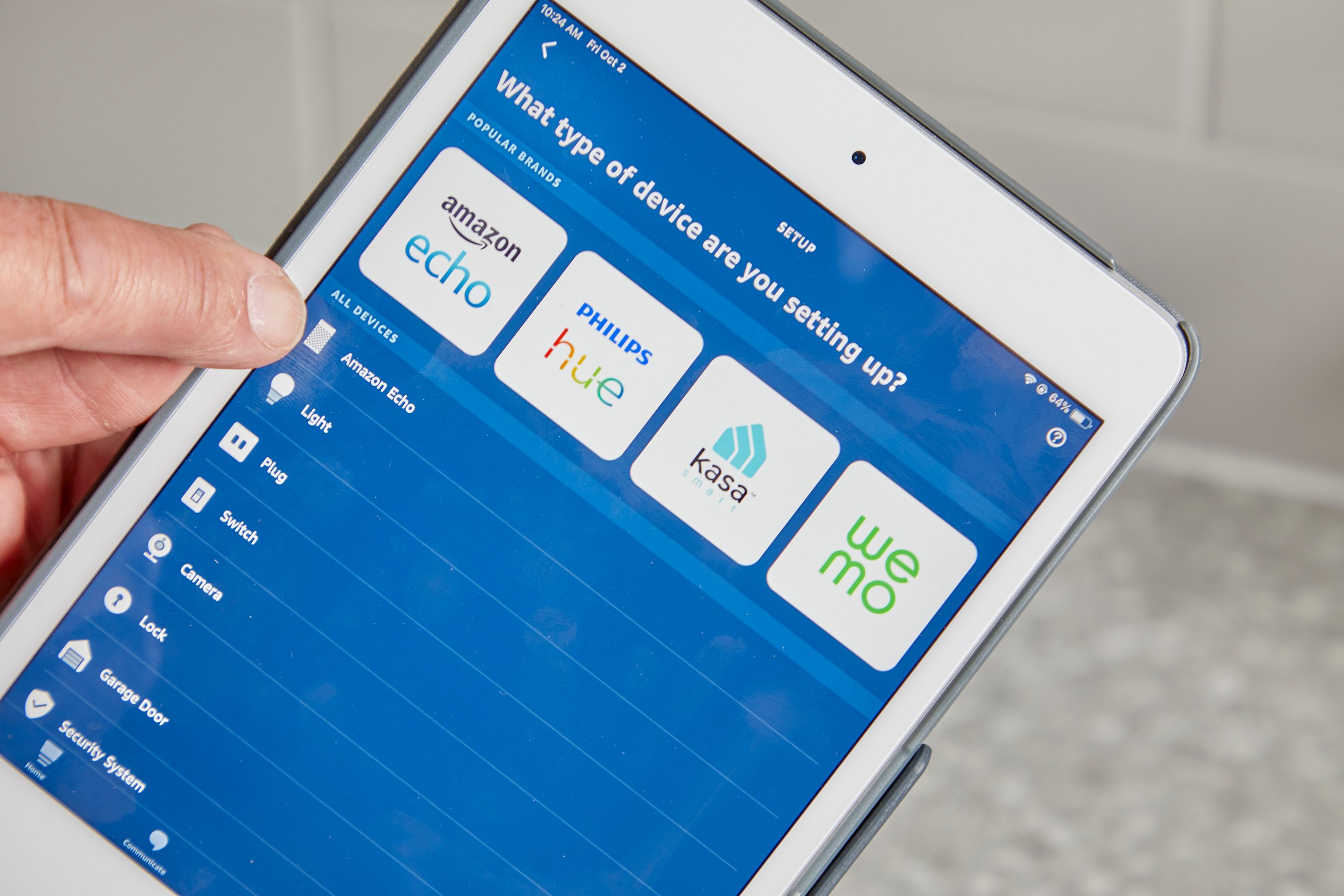 A hand interacts with a tablet displaying a setup screen for smart devices, featuring options for Amazon Echo, Philips Hue, and others.