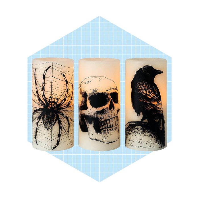 Three decorative candles, each adorned with distinct black illustrations: a spider, a skull, and a raven, set against a light blue grid background.