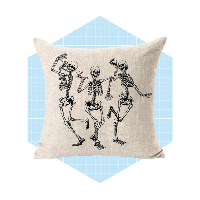 A decorative pillow features three dancing skeletons, each with a different pose, set against a light blue geometric background.