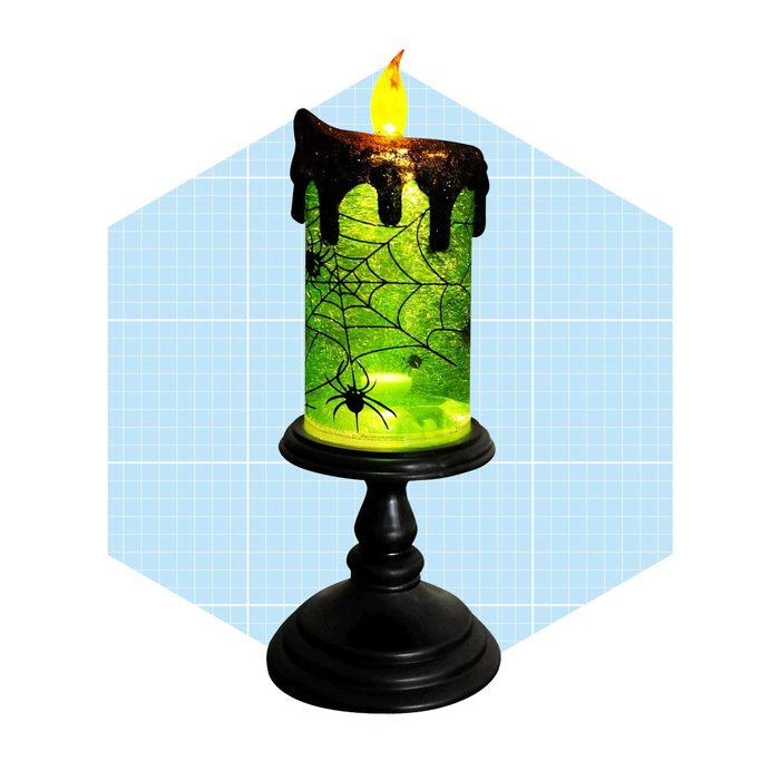 A decorative green candle flickers, featuring spider and web designs, placed on a black pedestal against a light blue grid background.