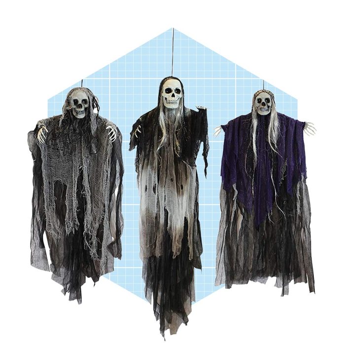 Three hanging skeleton figures wear tattered robes, each displaying a skull face and long hair, against a light blue, grid-patterned background.