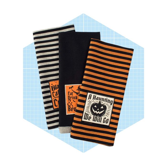 Three decorative towels featuring Halloween-themed designs and colors rest against a light blue grid background, featuring stripes and seasonal phrases.