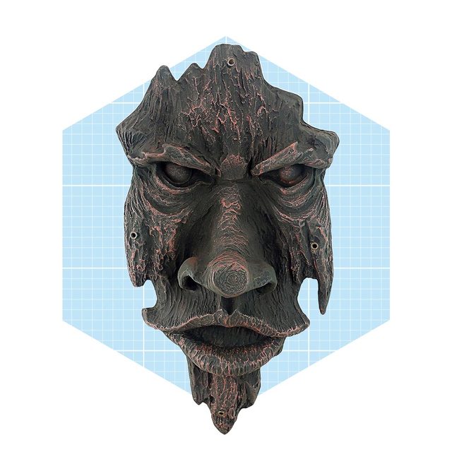 A wooden mask depicting a fierce face hangs against a light blue grid background, showcasing detailed textures and exaggerated facial features.