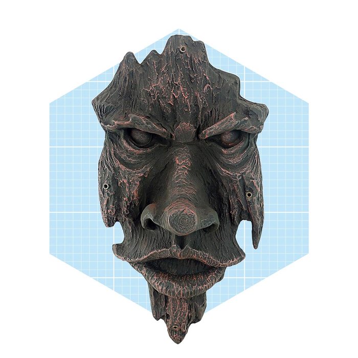 A wooden mask depicting a fierce face hangs against a light blue grid background, showcasing detailed textures and exaggerated facial features.