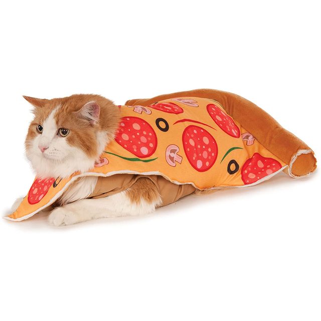 A cat lies calmly draped in a pizza-shaped blanket, featuring toppings like pepperoni and mushrooms, on a flat surface.