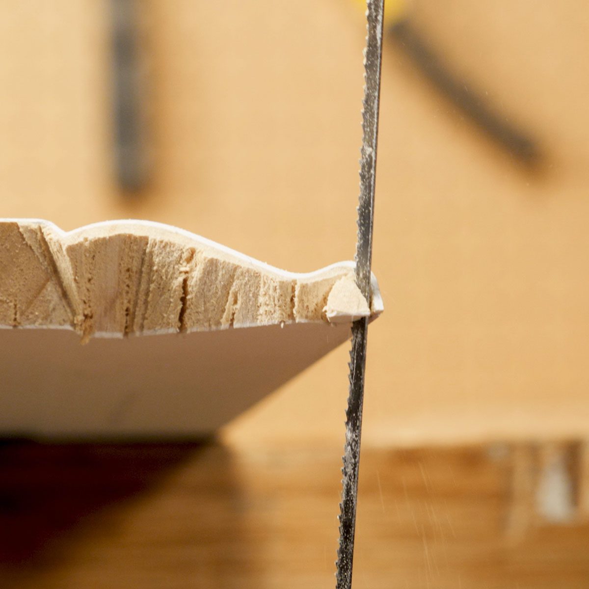 A hand saw cuts into a wooden piece, creating a textured edge, surrounded by a blurred background of workshop materials.