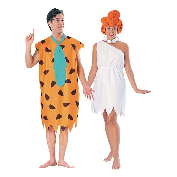 Two adults stand side by side, dressed in cartoonish prehistoric costumes; one in an orange tunic with spots, the other in a white dress and red hair.