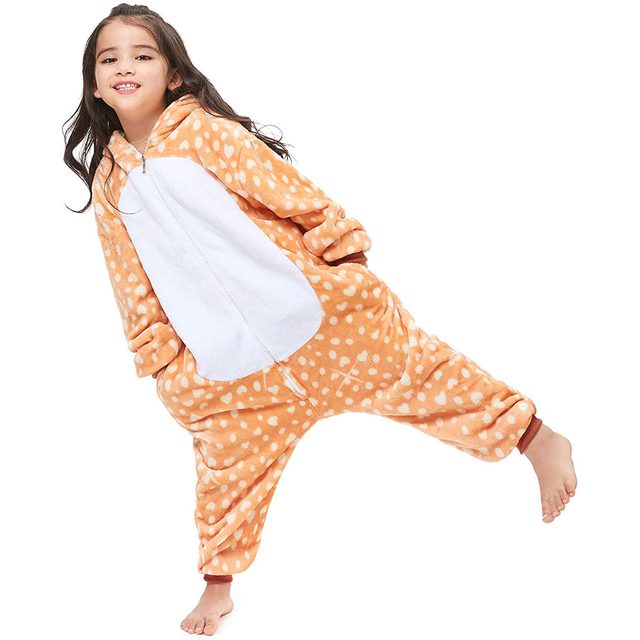 A girl in a spotted orange onesie playfully poses with one leg raised, smiling. The outfit resembles a deer, and she is barefoot.