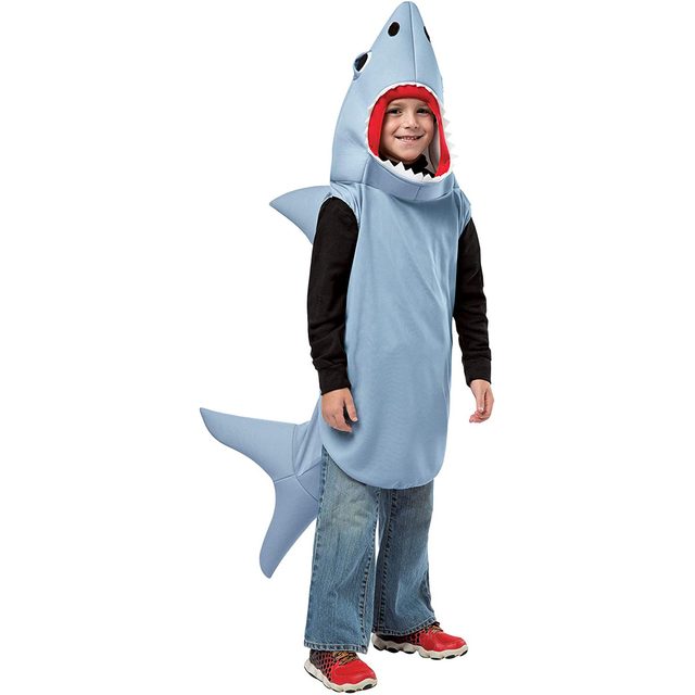 A child dressed in a blue shark costume stands smiling, with a red mouth and shark fin, against a plain white background.
