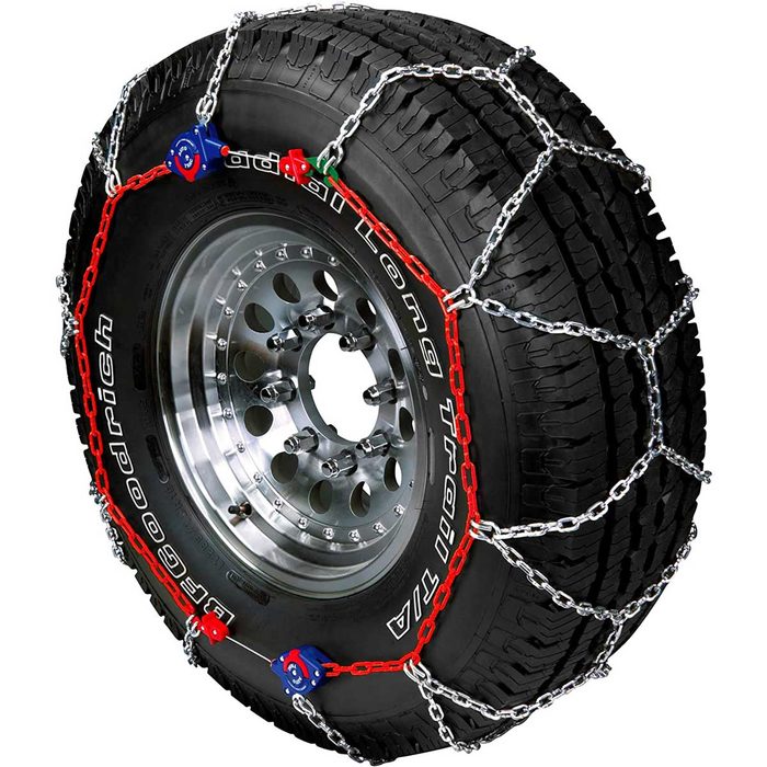 A tire equipped with a metal chain setup for enhanced traction sits against a smooth, metallic wheel, showcasing rugged tread and distinct lettering.