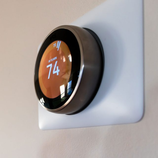 A digital thermostat displays a temperature of 74°F, indicating it will adjust in 15 minutes, mounted on a smooth, light-colored wall.