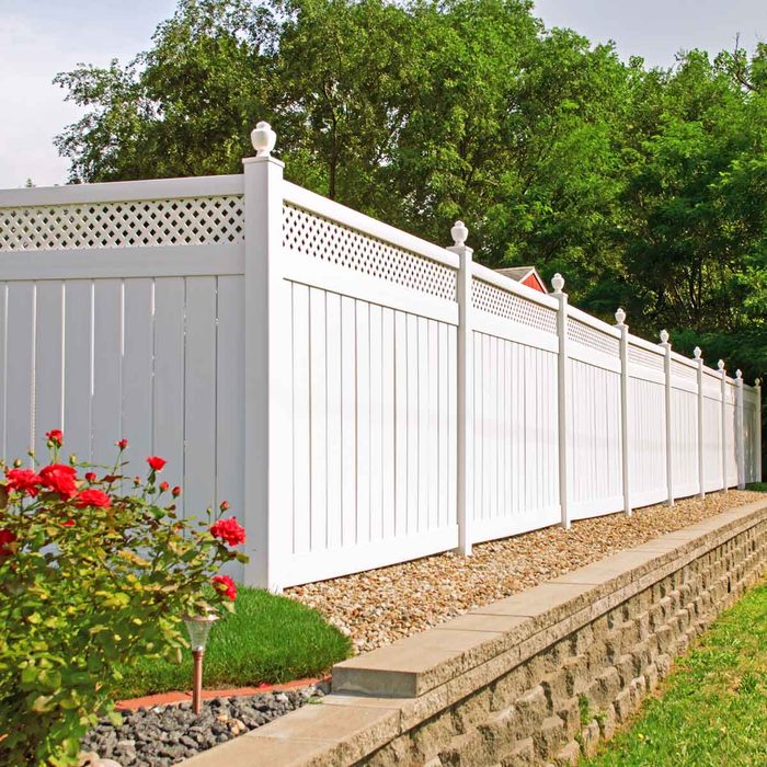 A white wooden fence lines a gravel pathway, bordered by colorful flowers and greenery, creating a tranquil outdoor space in a well-maintained yard.