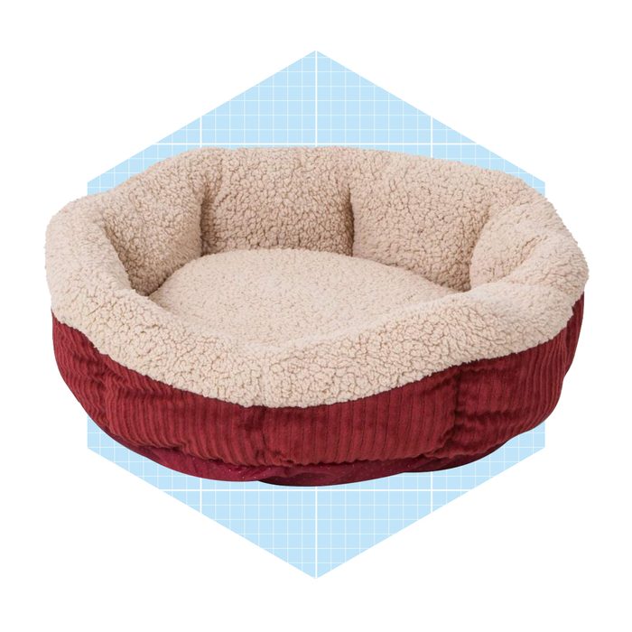 A round, plush pet bed features a soft cream interior and a textured red exterior, set against a light blue geometric background.