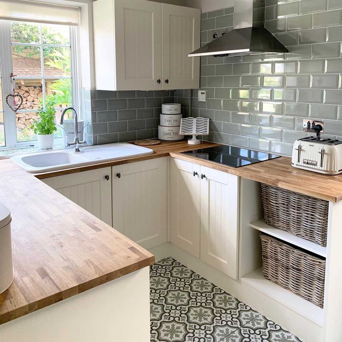 A well-lit kitchen features wooden countertops, a sink, a stove, and storage baskets. A window reveals greenery outside, adding natural light and warmth.