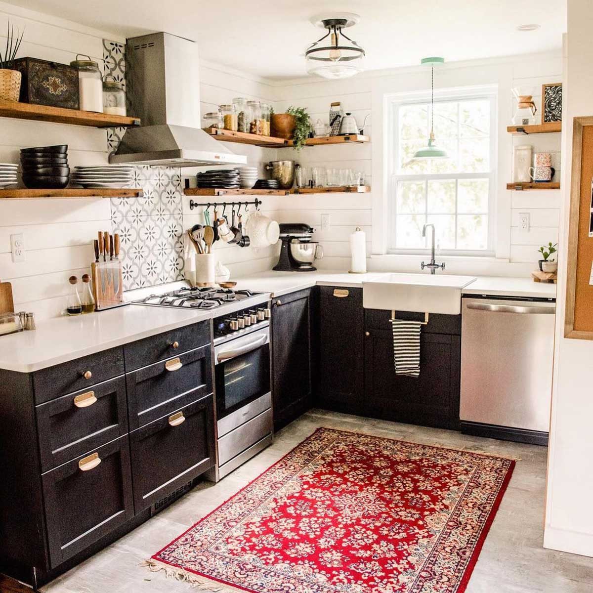 A modern kitchen features black cabinets, white countertops, a window above the sink, and a red patterned rug on the floor, creating a cozy environment.