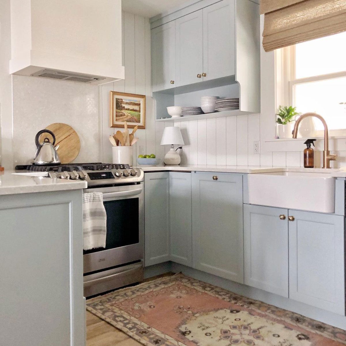 A pastel blue kitchen features a stainless steel stove, white sink, and decorative items. Natural light illuminates the space, creating a cozy atmosphere.