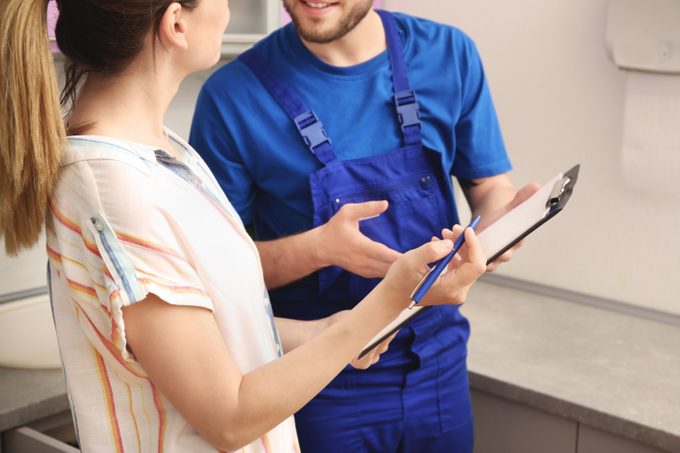 Professional plumber in uniform talking to client indoors