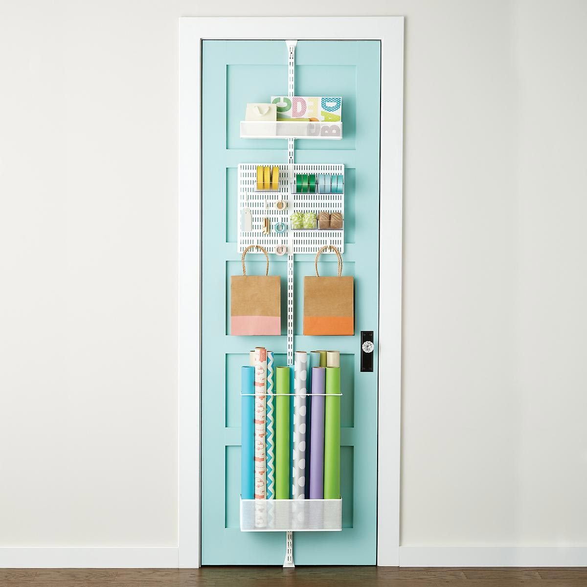 A turquoise door displays organized wrapping supplies, including rolls of paper and bags, stored in hanging compartments, enhancing space efficiency and accessibility.