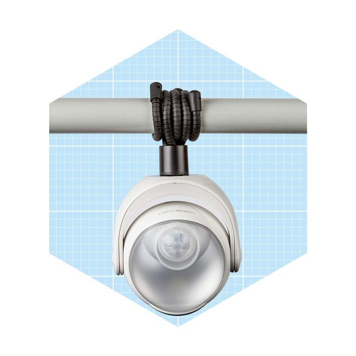 A spotlight is mounted on a pipe, illuminating a blue grid background, showcasing its design and functionality in an organized setting.