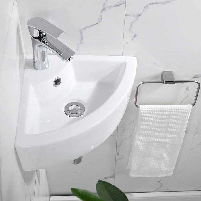 A corner sink features a modern faucet, draining water into a white basin, with a towel hanging nearby against a marbled wall.