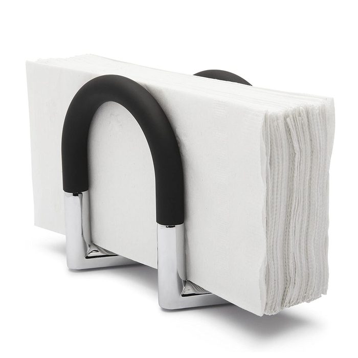 A napkin holder displays neatly stacked white napkins, secured by a curved black handle and chrome base, positioned on a flat surface.
