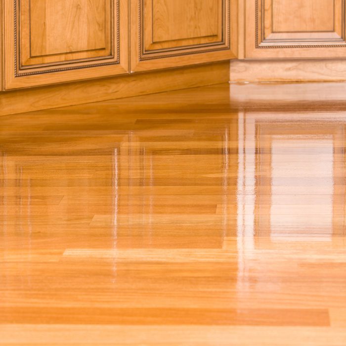 Polished hardwood flooring reflects light, showing a smooth surface. It meets wooden cabinetry at a corner, creating a warm, inviting interior space.