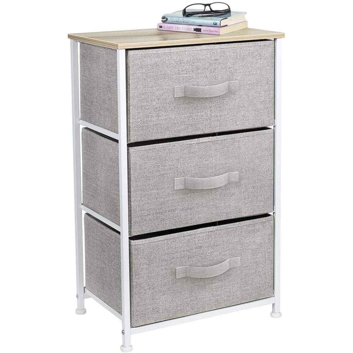 A three-drawer storage unit with a wooden top and gray fabric drawers sits in a room, holding books and glasses on its surface.