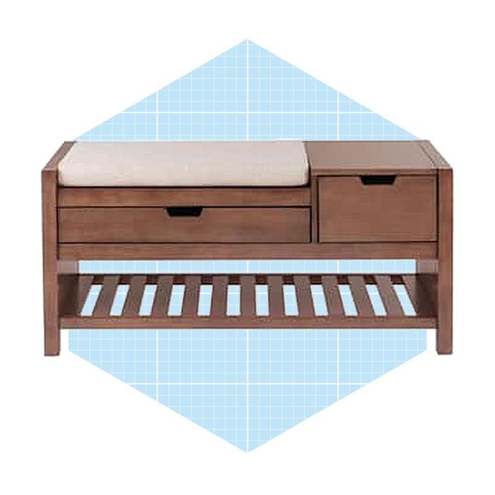 A wooden bench with a cushioned top rests on a slatted base, featuring two drawers for storage, set against a light blue geometric background.