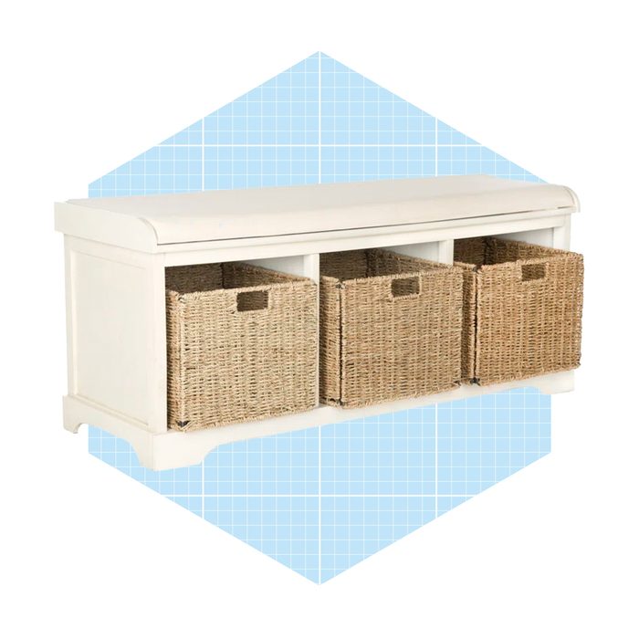 A white storage bench with three woven baskets is positioned on a blue grid-patterned background, designed for organization in a home environment.
