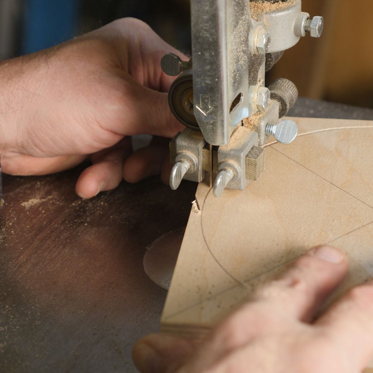 A hand guides a cutting tool along a marked wooden piece, shaping it while sawdust collects on a smooth work surface in a workshop.