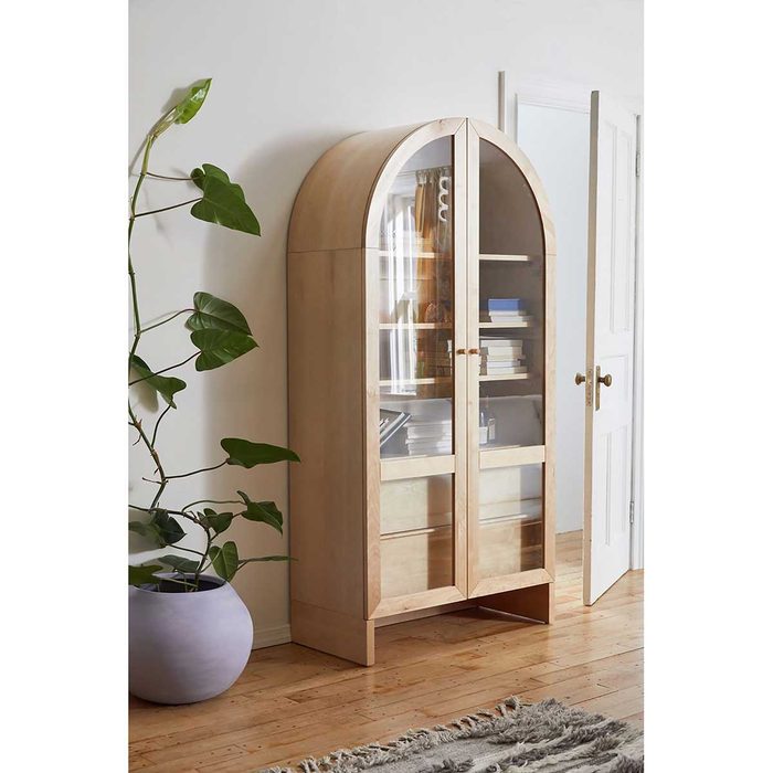 A wooden display cabinet stands against a wall, holding books. A potted plant and an open door add to the cozy interior ambiance.