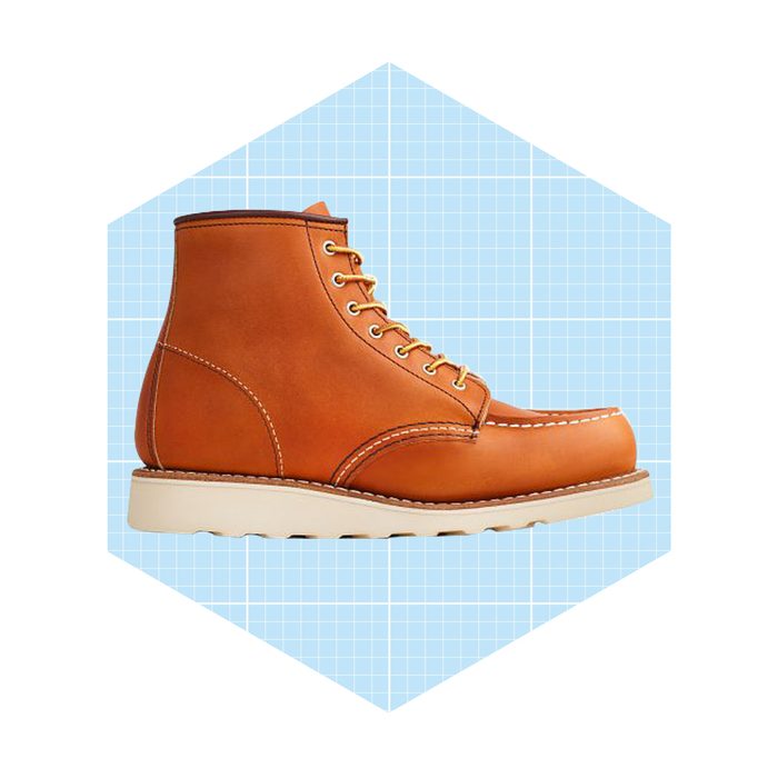 A brown leather boot stands upright, featuring gold eyelets and white soles, against a light blue grid background.