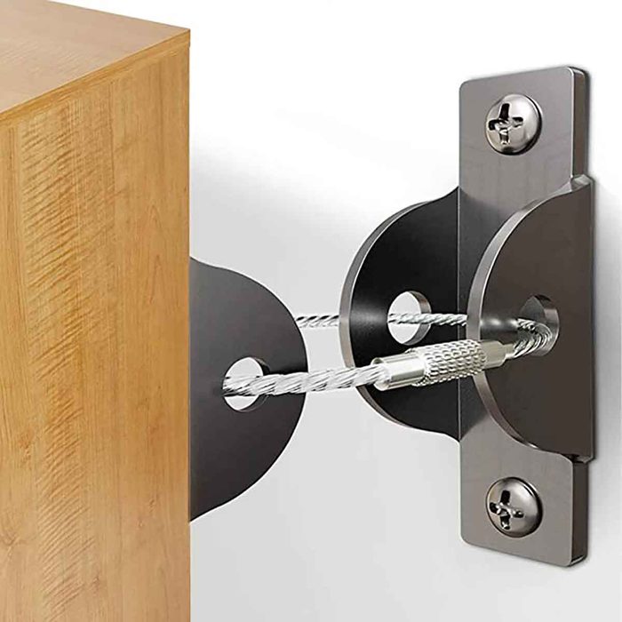 A wooden corner is secured to a wall with a black metal bracket and a cable; the setup prevents movement of the furniture piece.