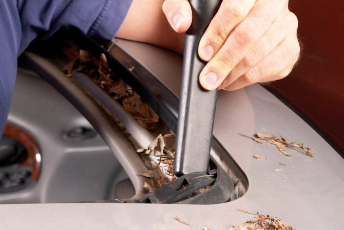 A person uses a tool to clean leaves from a car's roof seam, ensuring proper maintenance in a detailed automotive context.