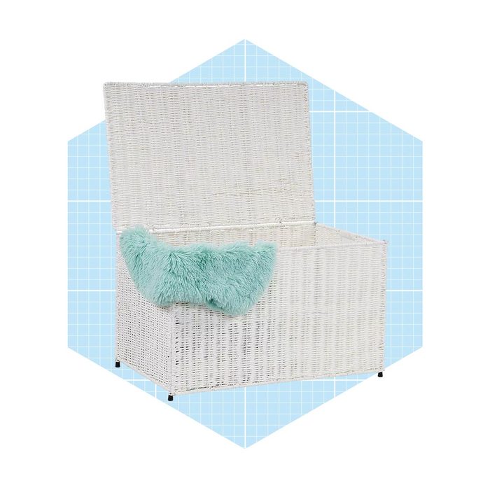 A white wicker storage chest sits open, revealing an empty interior. A fluffy turquoise cushion rests inside, set against a light blue grid background.